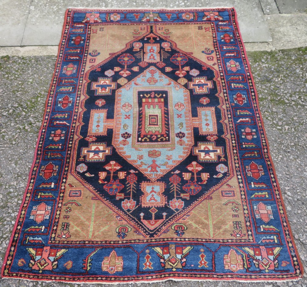 An antique hand-knotted Persian Hamadan wool rug featuring a central geometric medallion in navy and light blue framed by a tan field and patterned blue borders.