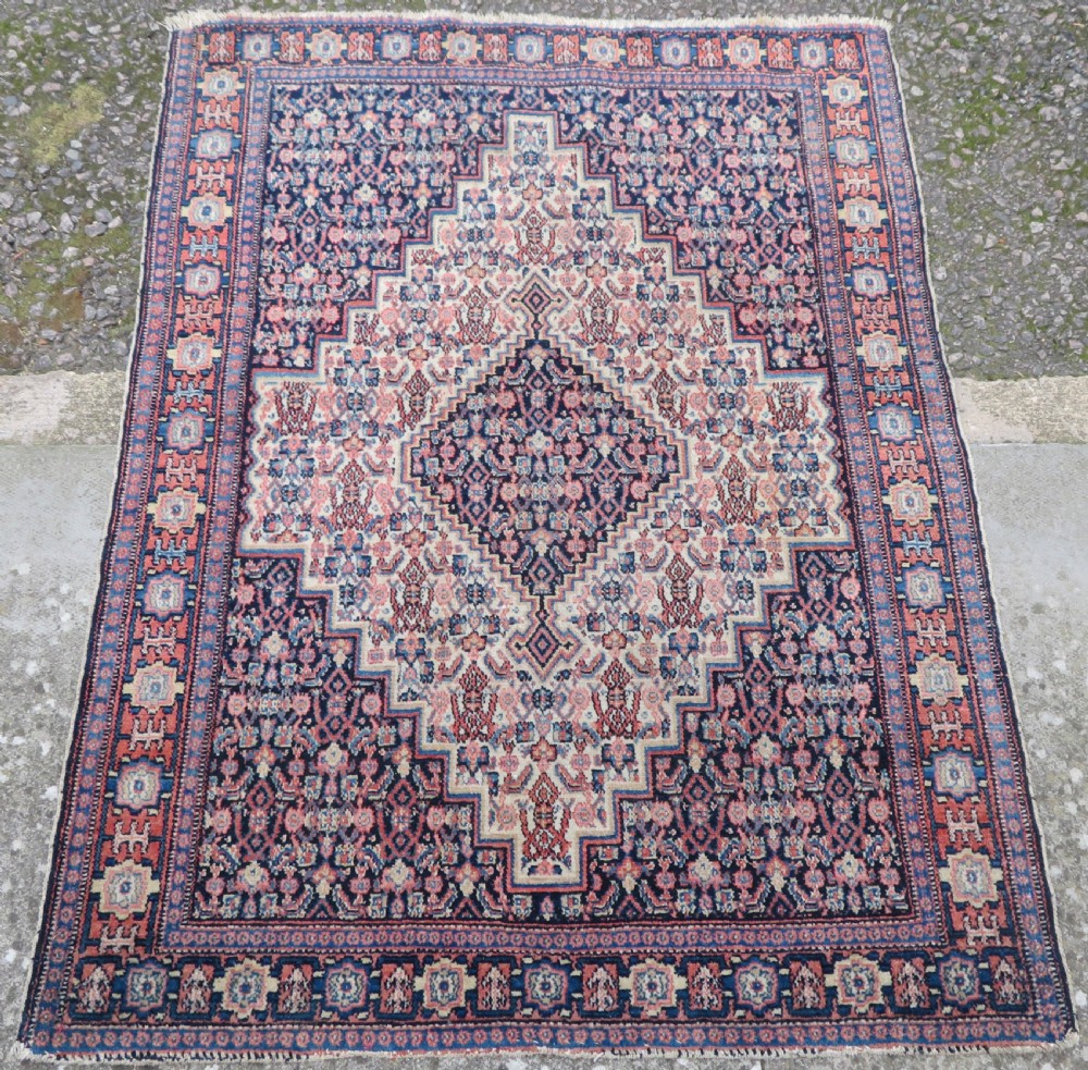 An antique Kurdish Senneh hand-knotted wool rug featuring a central stepped diamond medallion surrounded by detailed repeating motifs in navy blue, terracotta red, and cream. View II