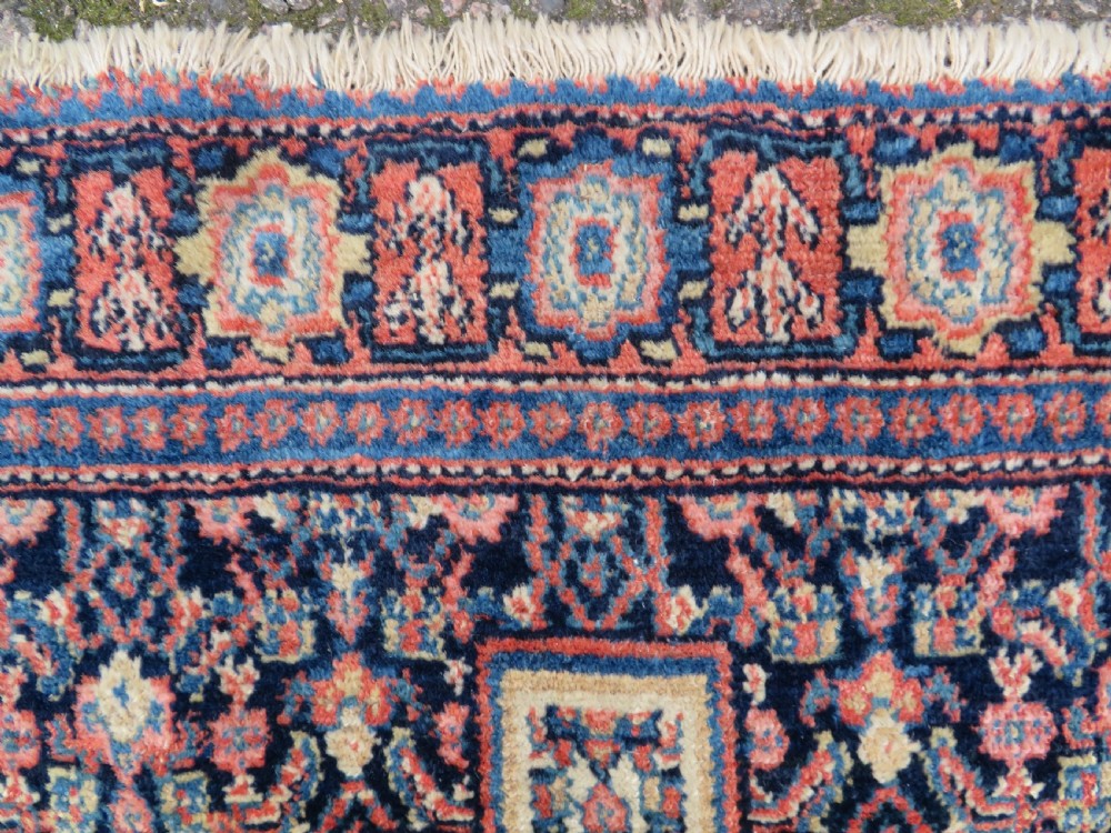 An antique Kurdish Senneh hand-knotted wool rug featuring a central stepped diamond medallion surrounded by detailed repeating motifs in navy blue, terracotta red, and cream. View VII