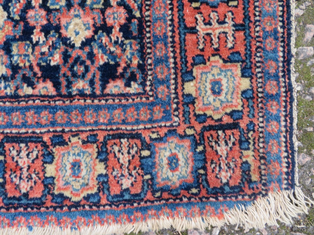 An antique Kurdish Senneh hand-knotted wool rug featuring a central stepped diamond medallion surrounded by detailed repeating motifs in navy blue, terracotta red, and cream. View IX