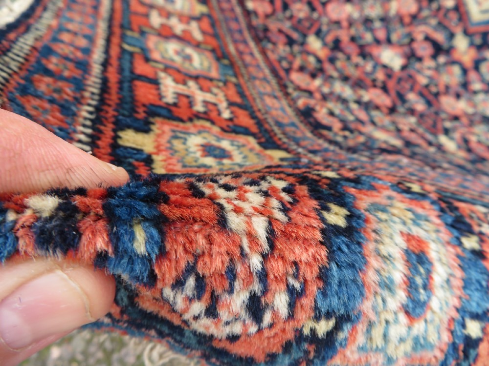 An antique Kurdish Senneh hand-knotted wool rug featuring a central stepped diamond medallion surrounded by detailed repeating motifs in navy blue, terracotta red, and cream. View XII