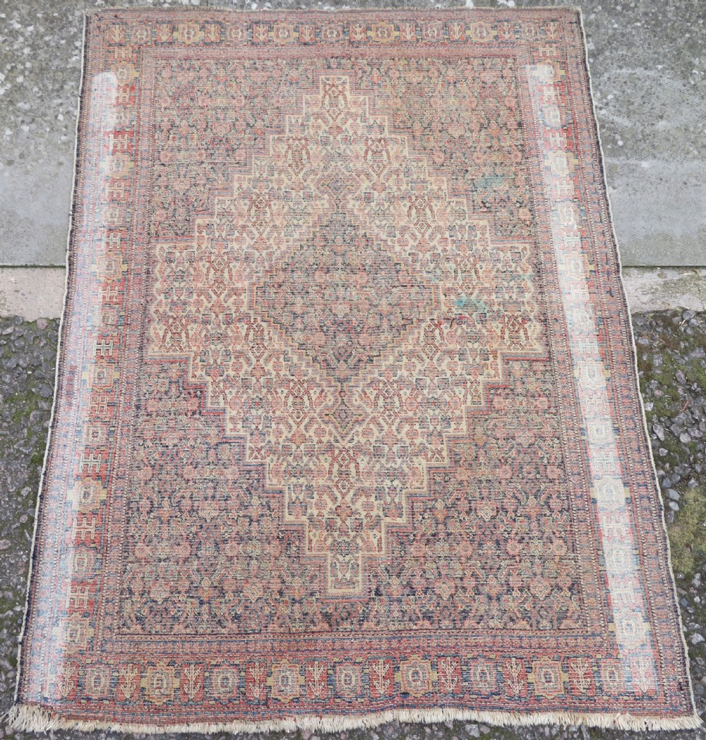 An antique Kurdish Senneh hand-knotted wool rug featuring a central stepped diamond medallion surrounded by detailed repeating motifs in navy blue, terracotta red, and cream. View XIV
