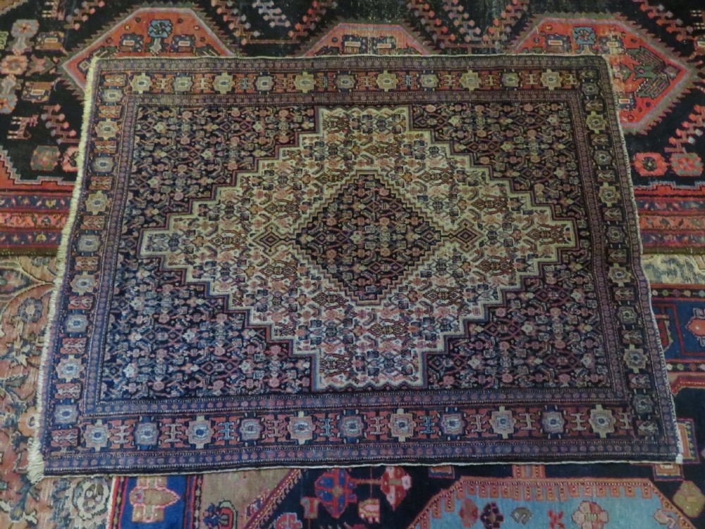 An antique Kurdish Senneh hand-knotted wool rug featuring a central stepped diamond medallion surrounded by detailed repeating motifs in navy blue, terracotta red, and cream. View XIX