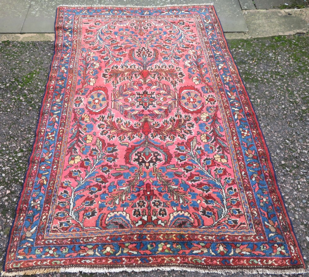 An antique Persian Sarouk hand-knotted wool rug featuring a central floral medallion surrounded by intricate floral vine patterns in rose pink, light blue, navy, and ivory hues.