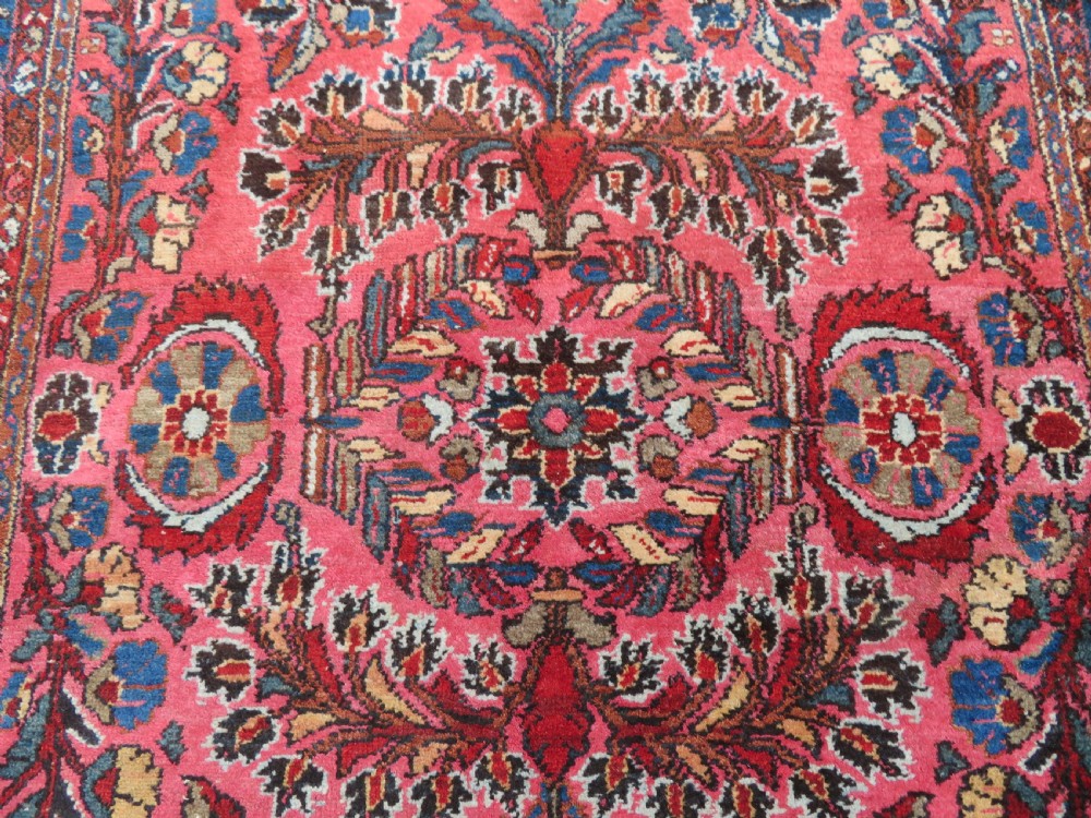 An antique Persian Sarouk hand-knotted wool rug featuring a central floral medallion surrounded by intricate floral vine patterns in rose pink, light blue, navy, and ivory hues. View III