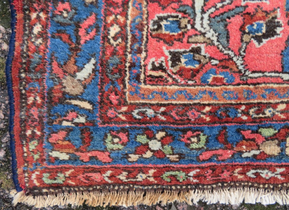 An antique Persian Sarouk hand-knotted wool rug featuring a central floral medallion surrounded by intricate floral vine patterns in rose pink, light blue, navy, and ivory hues. View VI