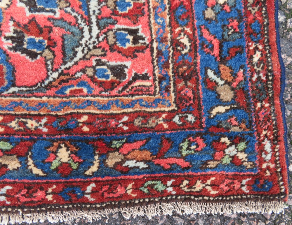 An antique Persian Sarouk hand-knotted wool rug featuring a central floral medallion surrounded by intricate floral vine patterns in rose pink, light blue, navy, and ivory hues. View VII
