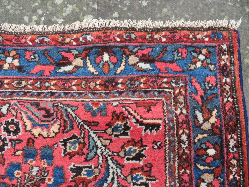 An antique Persian Sarouk hand-knotted wool rug featuring a central floral medallion surrounded by intricate floral vine patterns in rose pink, light blue, navy, and ivory hues. View VIII