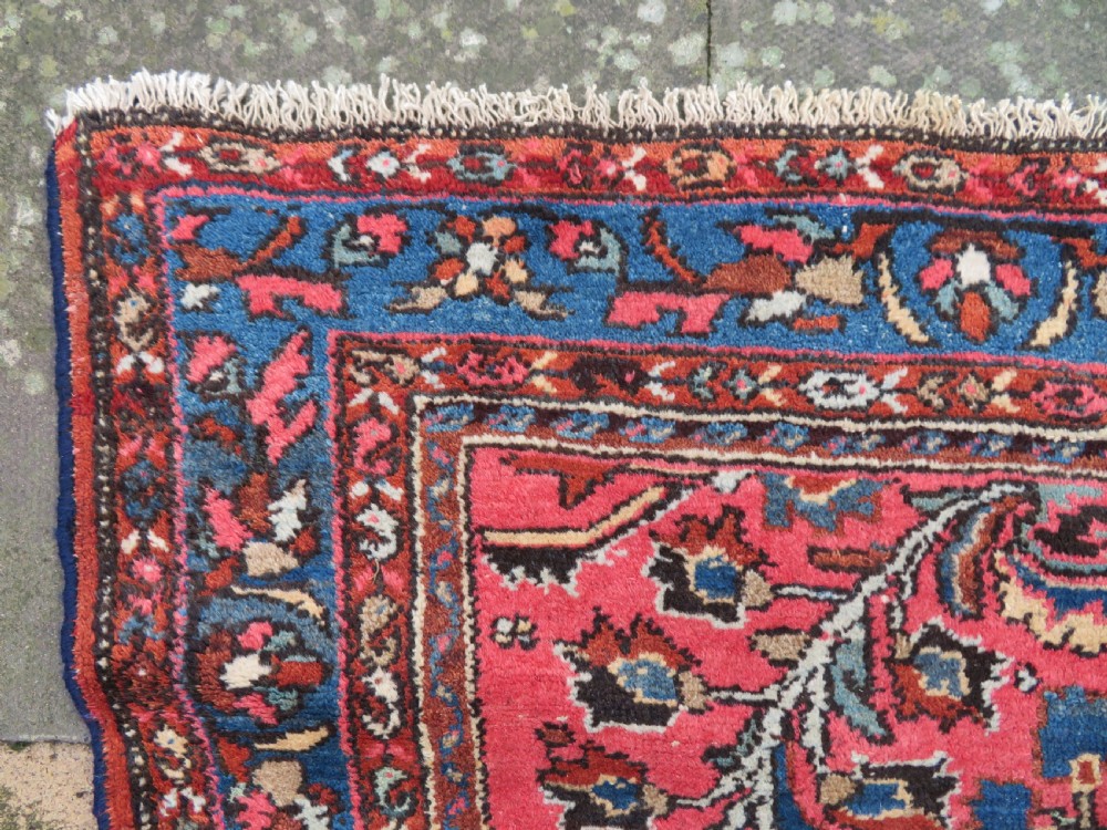 An antique Persian Sarouk hand-knotted wool rug featuring a central floral medallion surrounded by intricate floral vine patterns in rose pink, light blue, navy, and ivory hues. View IX