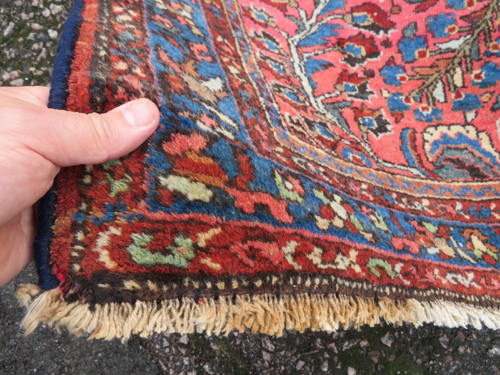 An antique Persian Sarouk hand-knotted wool rug featuring a central floral medallion surrounded by intricate floral vine patterns in rose pink, light blue, navy, and ivory hues. View X