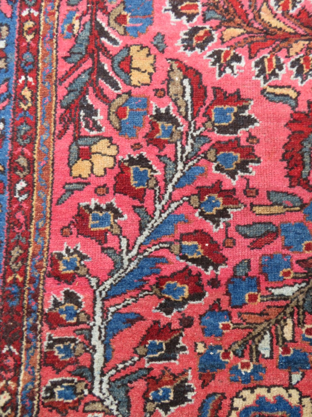 An antique Persian Sarouk hand-knotted wool rug featuring a central floral medallion surrounded by intricate floral vine patterns in rose pink, light blue, navy, and ivory hues. View XIV
