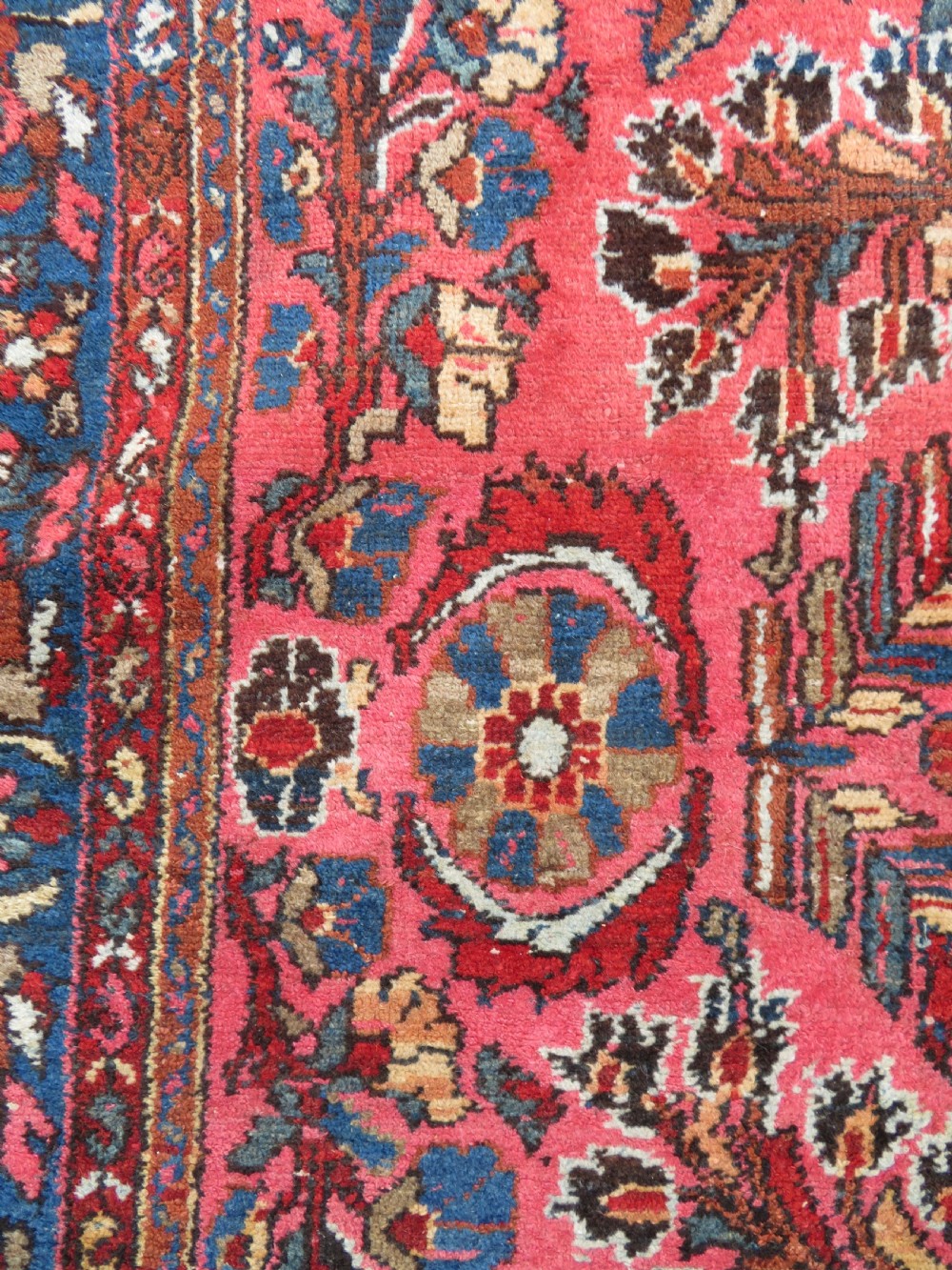 An antique Persian Sarouk hand-knotted wool rug featuring a central floral medallion surrounded by intricate floral vine patterns in rose pink, light blue, navy, and ivory hues. View XV