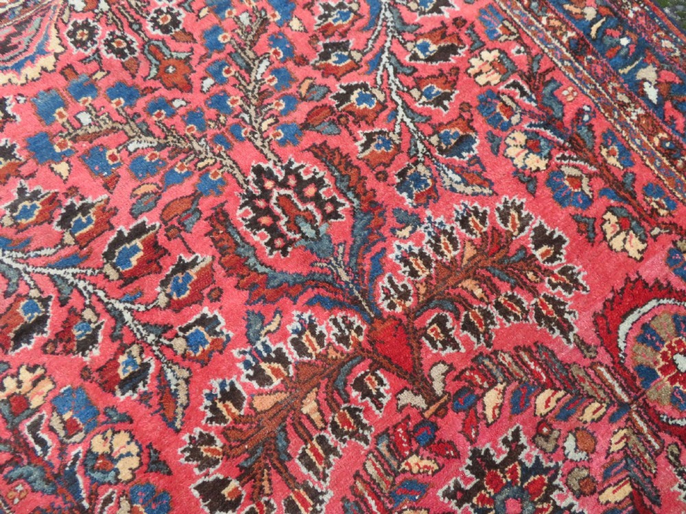 An antique Persian Sarouk hand-knotted wool rug featuring a central floral medallion surrounded by intricate floral vine patterns in rose pink, light blue, navy, and ivory hues. View XVI