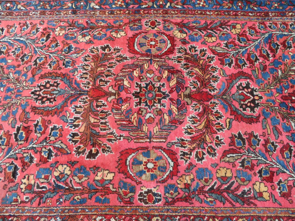 An antique Persian Sarouk hand-knotted wool rug featuring a central floral medallion surrounded by intricate floral vine patterns in rose pink, light blue, navy, and ivory hues. View XVII