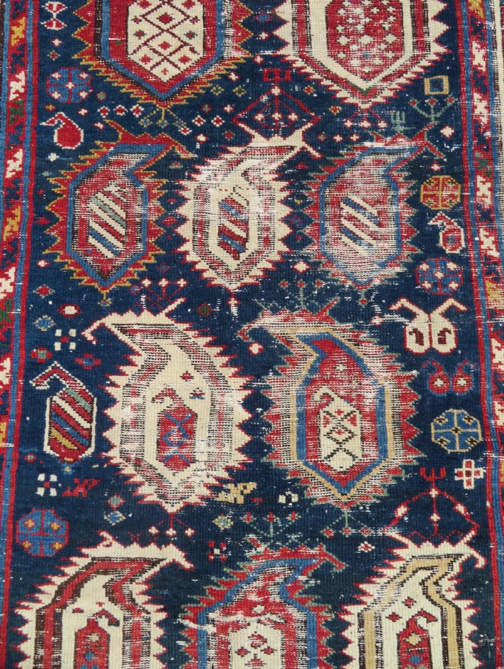 An antique Caucasian Kazak wool runner rug with repeating boteh motifs on a navy blue field framed by geometric multicoloured borders. View III