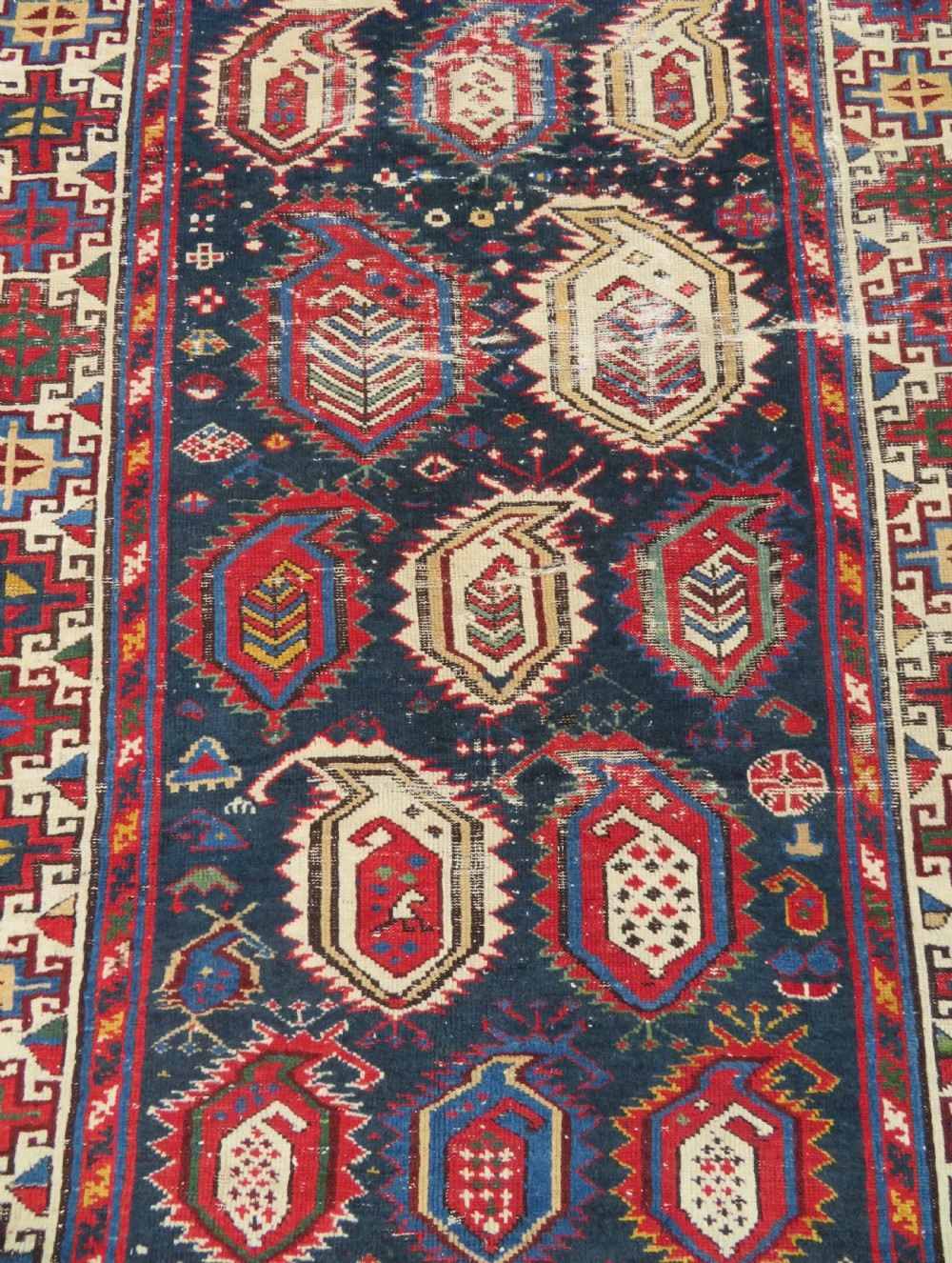 An antique Caucasian Kazak wool runner rug with repeating boteh motifs on a navy blue field framed by geometric multicoloured borders. View VI