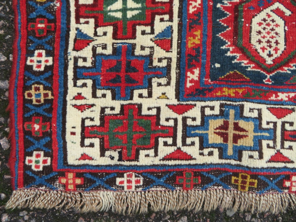 An antique Caucasian Kazak wool runner rug with repeating boteh motifs on a navy blue field framed by geometric multicoloured borders. View VII