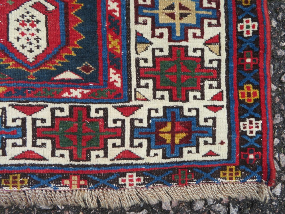 An antique Caucasian Kazak wool runner rug with repeating boteh motifs on a navy blue field framed by geometric multicoloured borders. View IX