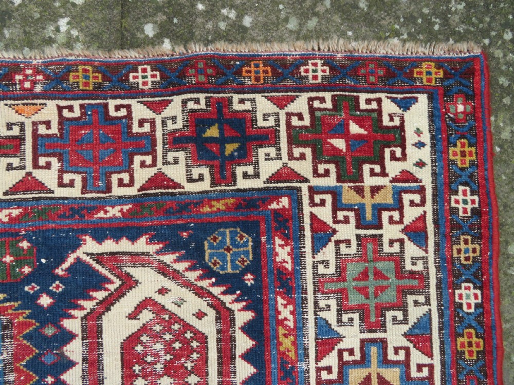 An antique Caucasian Kazak wool runner rug with repeating boteh motifs on a navy blue field framed by geometric multicoloured borders. View X