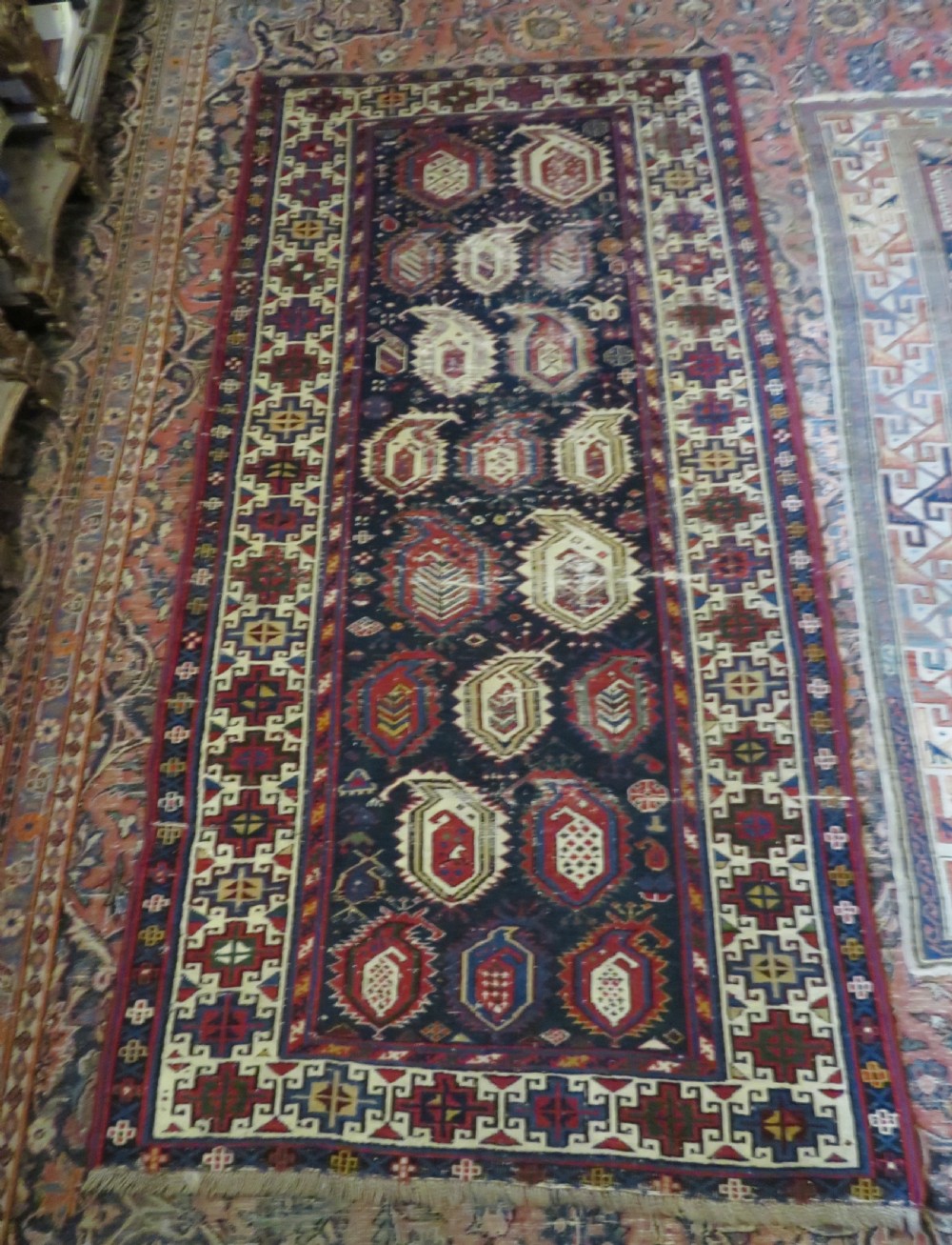 An antique Caucasian Kazak wool runner rug with repeating boteh motifs on a navy blue field framed by geometric multicoloured borders. View XIX