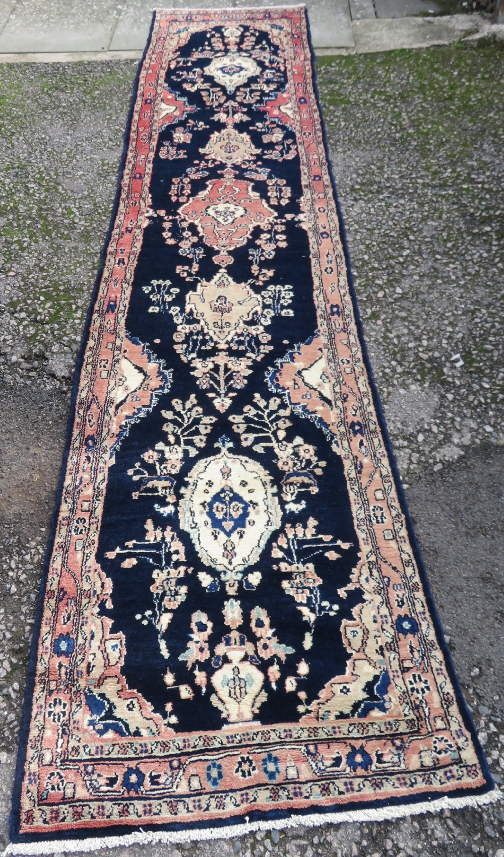 A long, narrow hand-knotted Persian Sarouk runner rug featuring a deep navy blue field, central floral medallions, and terracotta borders.