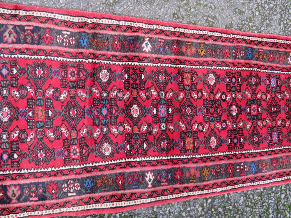 A long, narrow hand-knotted Persian Hamadan runner rug featuring a red field woven with geometric motifs and dark patterned borders. View VI