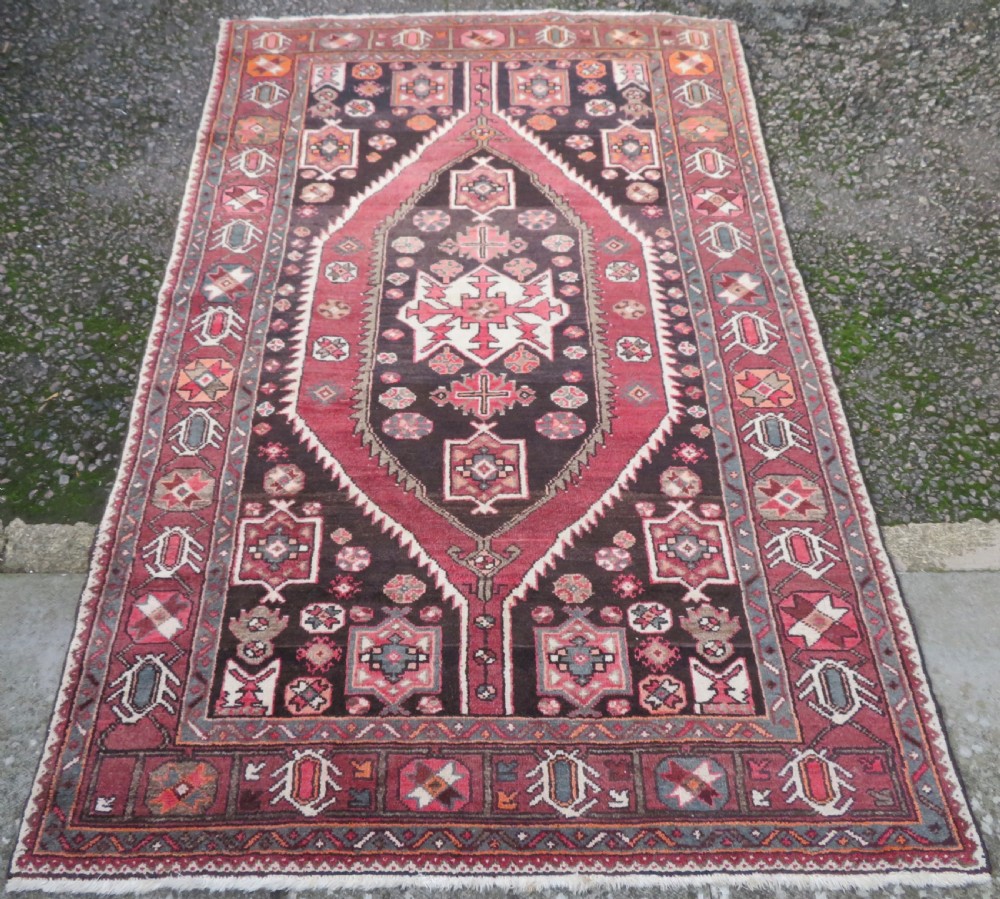 A rectangular hand-knotted North West Persian Kurdish wool rug featuring a central crimson diamond medallion surrounded by geometric motifs on a dark brown field with decorative borders. View II