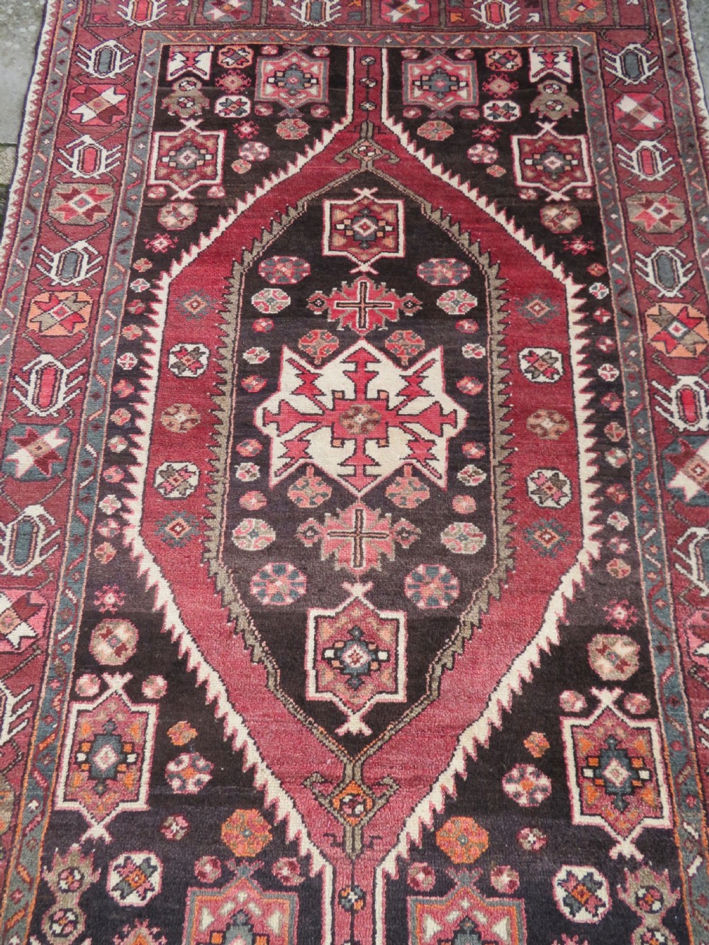 A rectangular hand-knotted North West Persian Kurdish wool rug featuring a central crimson diamond medallion surrounded by geometric motifs on a dark brown field with decorative borders. View III