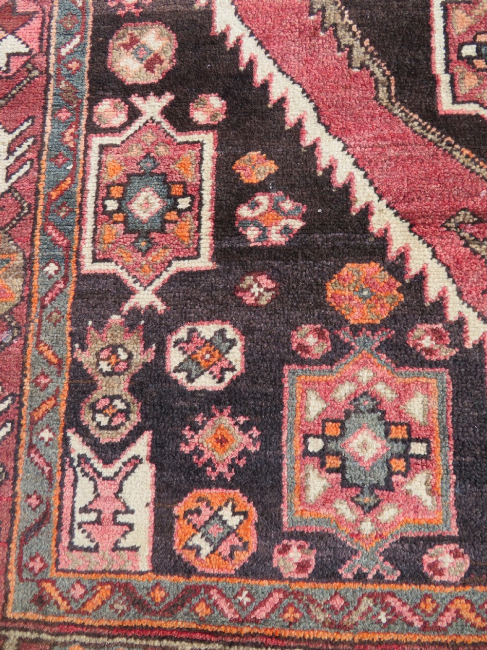 A rectangular hand-knotted North West Persian Kurdish wool rug featuring a central crimson diamond medallion surrounded by geometric motifs on a dark brown field with decorative borders. View VII