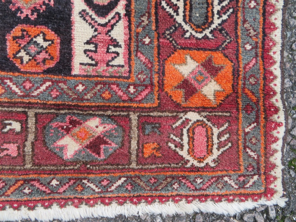 A rectangular hand-knotted North West Persian Kurdish wool rug featuring a central crimson diamond medallion surrounded by geometric motifs on a dark brown field with decorative borders. View IX
