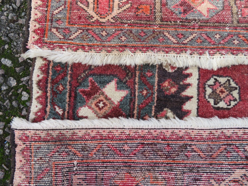 A rectangular hand-knotted North West Persian Kurdish wool rug featuring a central crimson diamond medallion surrounded by geometric motifs on a dark brown field with decorative borders. View XV