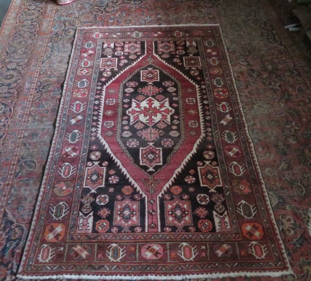 A rectangular hand-knotted North West Persian Kurdish wool rug featuring a central crimson diamond medallion surrounded by geometric motifs on a dark brown field with decorative borders. View XVII