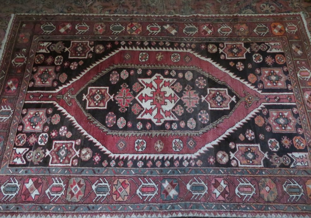 A rectangular hand-knotted North West Persian Kurdish wool rug featuring a central crimson diamond medallion surrounded by geometric motifs on a dark brown field with decorative borders. View XVIII