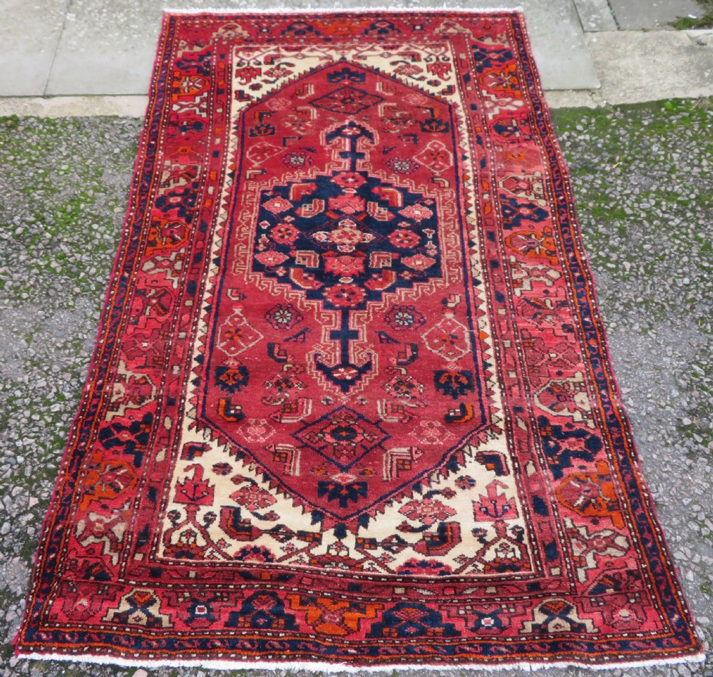 An antique Persian Malayer hand-knotted wool rug featuring a red central field, stepped navy medallion, ivory spandrels, and geometric floral borders.
