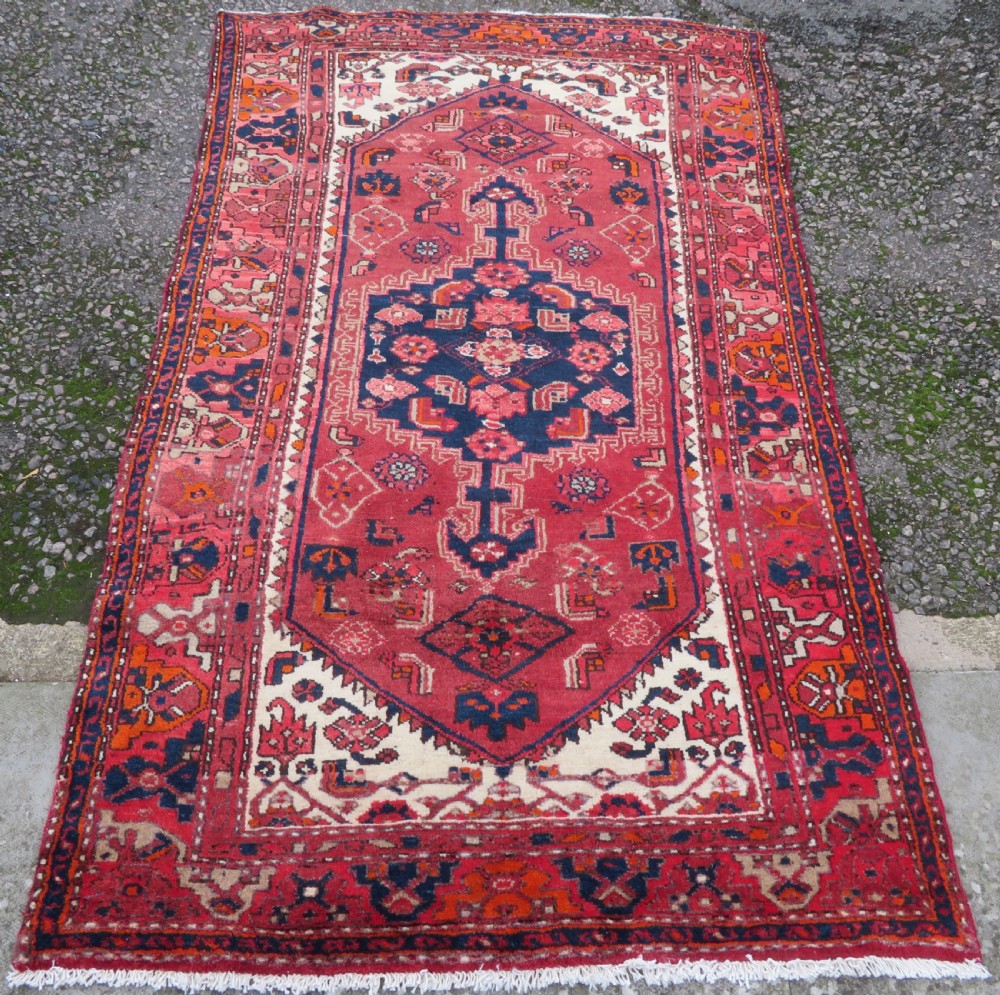 An antique Persian Malayer hand-knotted wool rug featuring a red central field, stepped navy medallion, ivory spandrels, and geometric floral borders. View II