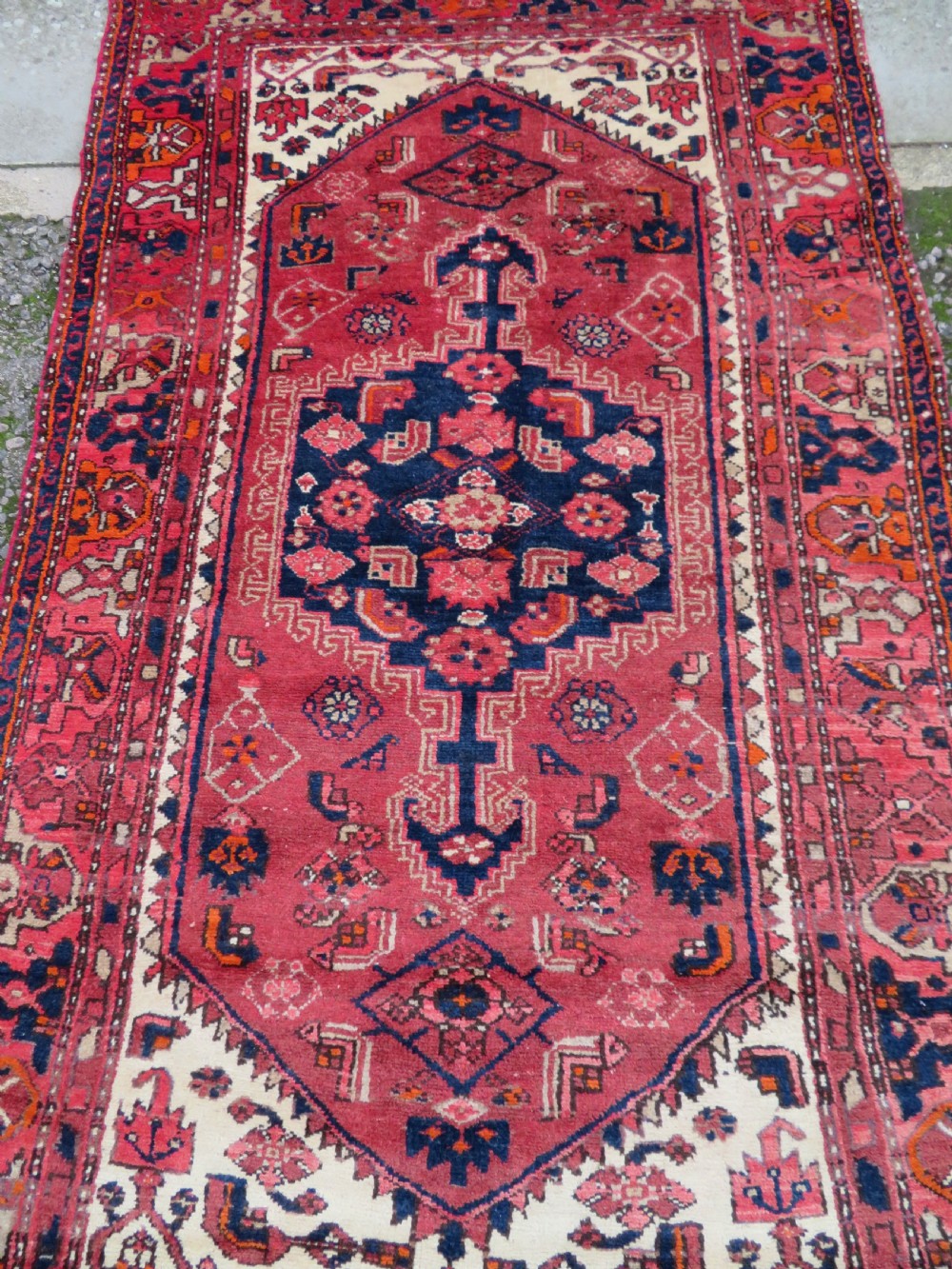 An antique Persian Malayer hand-knotted wool rug featuring a red central field, stepped navy medallion, ivory spandrels, and geometric floral borders. View III