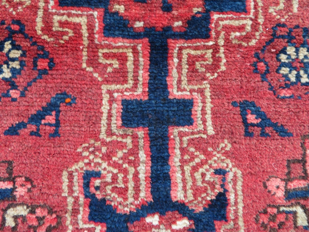 An antique Persian Malayer hand-knotted wool rug featuring a red central field, stepped navy medallion, ivory spandrels, and geometric floral borders. View V