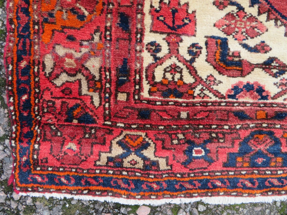 An antique Persian Malayer hand-knotted wool rug featuring a red central field, stepped navy medallion, ivory spandrels, and geometric floral borders. View VII