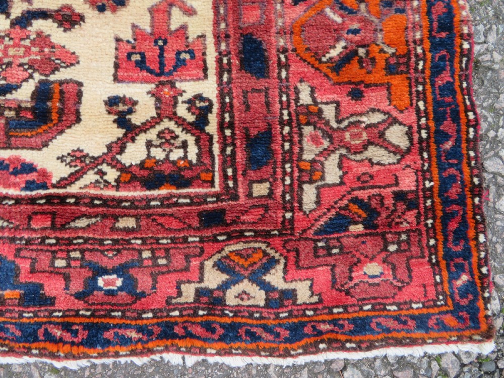 An antique Persian Malayer hand-knotted wool rug featuring a red central field, stepped navy medallion, ivory spandrels, and geometric floral borders. View VIII