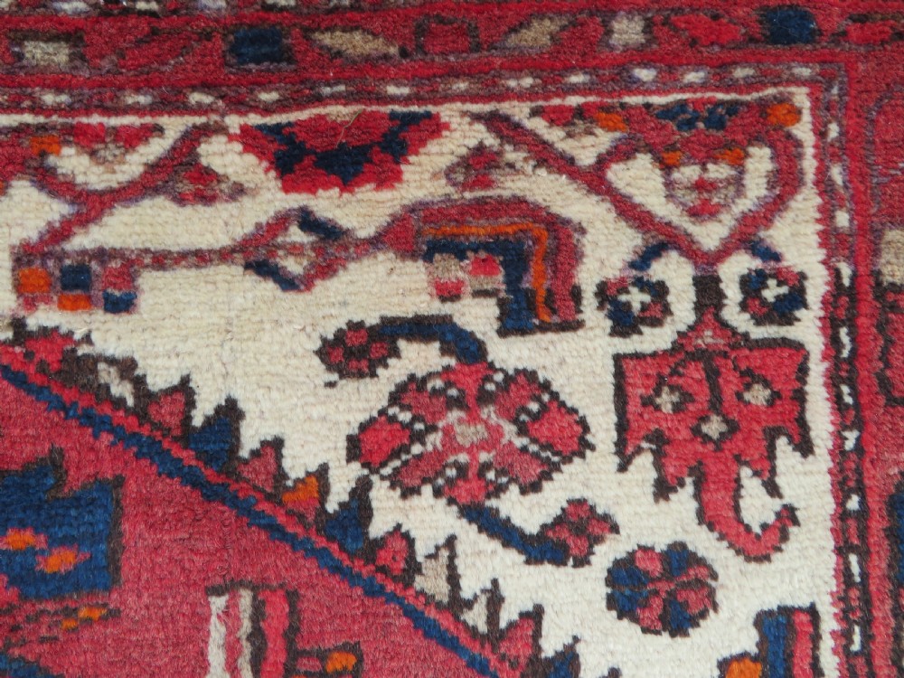 An antique Persian Malayer hand-knotted wool rug featuring a red central field, stepped navy medallion, ivory spandrels, and geometric floral borders. View XI