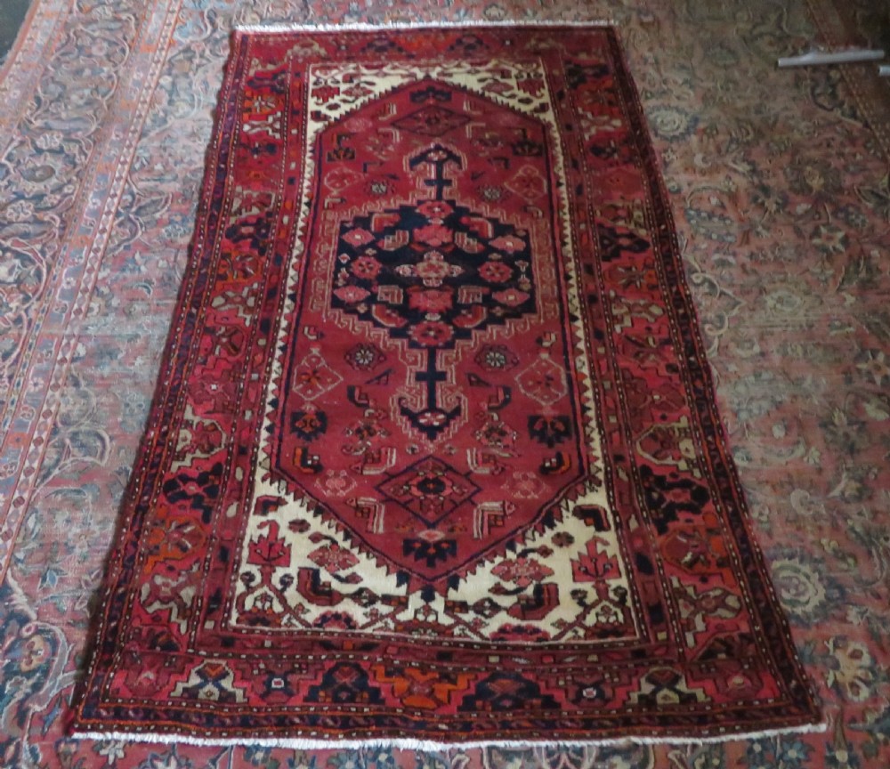 An antique Persian Malayer hand-knotted wool rug featuring a red central field, stepped navy medallion, ivory spandrels, and geometric floral borders. View XVIII