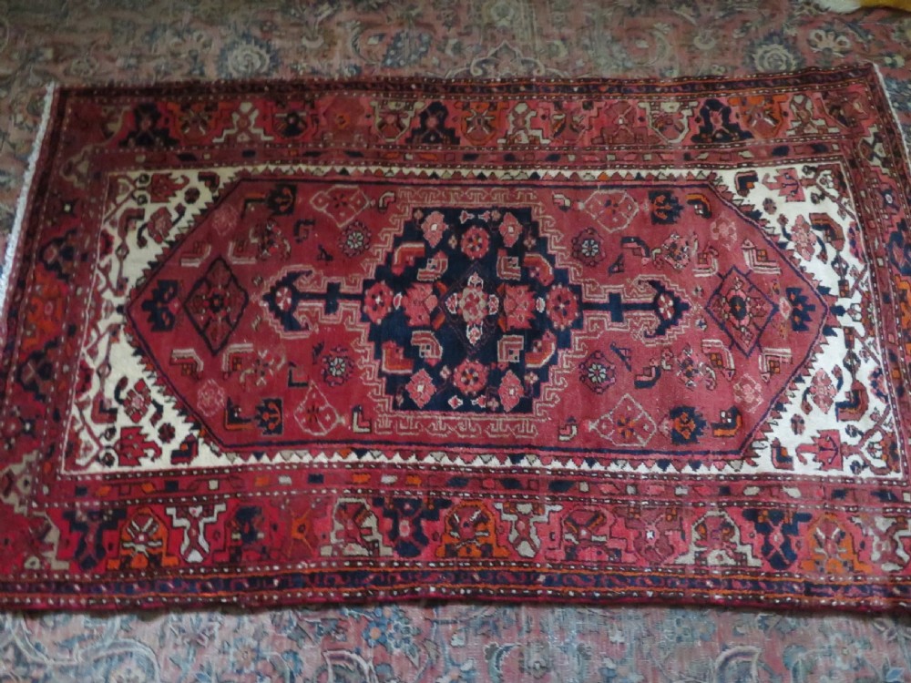 An antique Persian Malayer hand-knotted wool rug featuring a red central field, stepped navy medallion, ivory spandrels, and geometric floral borders. View XIX