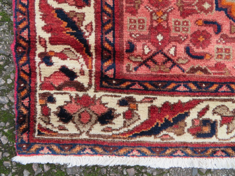 An antique Persian Sanjan Hamadan wool rug runner featuring a central diamond medallion surrounded by geometric motifs in red, cream, and navy blue. View V