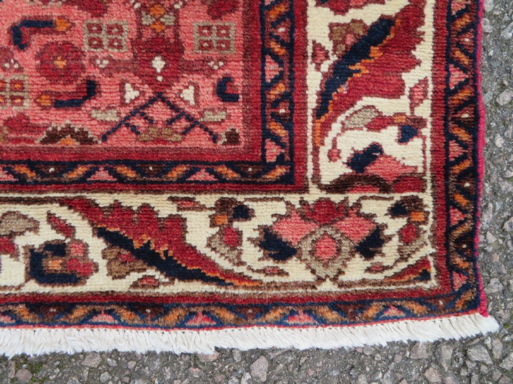 An antique Persian Sanjan Hamadan wool rug runner featuring a central diamond medallion surrounded by geometric motifs in red, cream, and navy blue. View VI