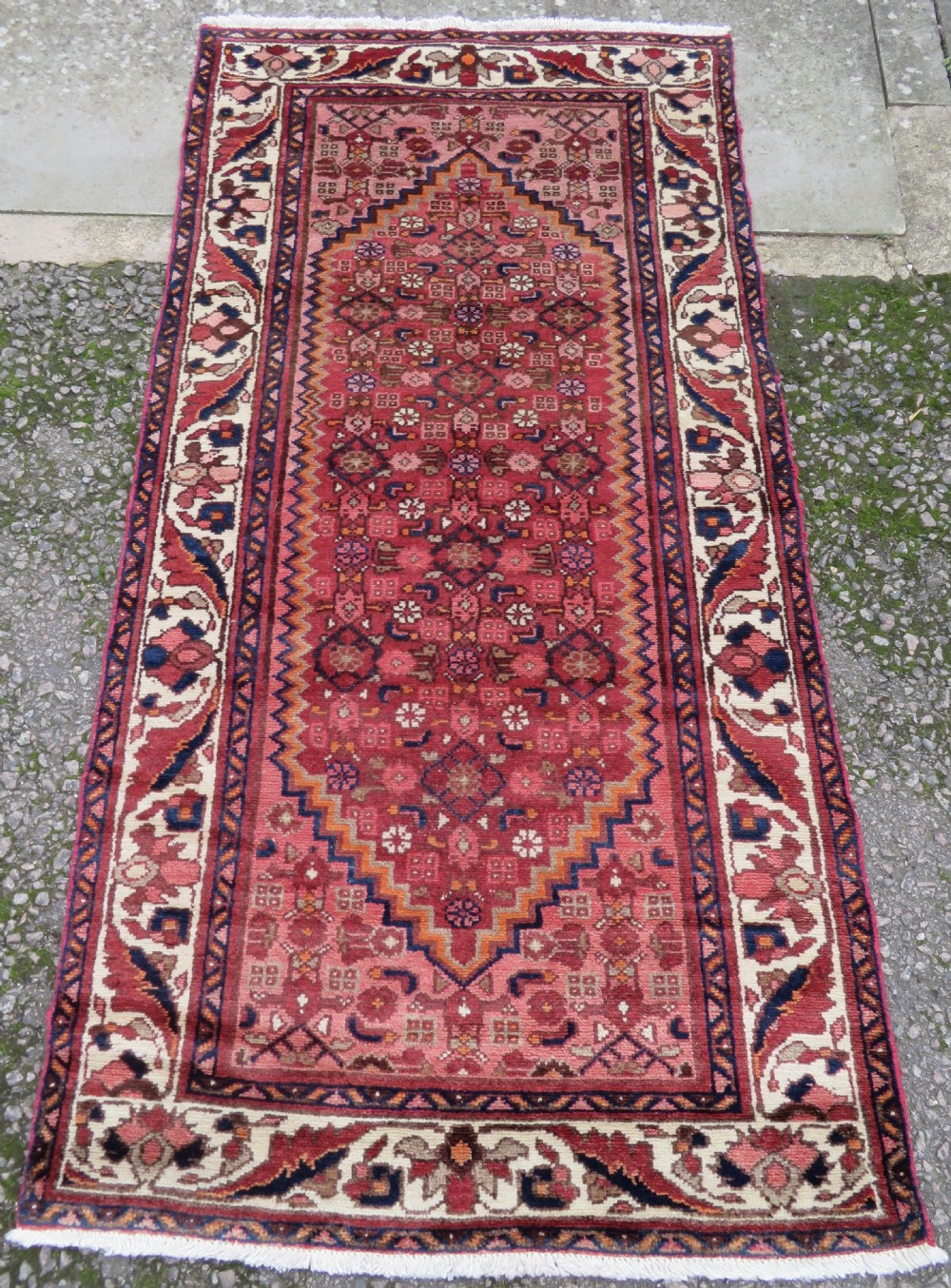 An antique Persian Sanjan Hamadan wool rug runner featuring a central diamond medallion surrounded by geometric motifs in red, cream, and navy blue.