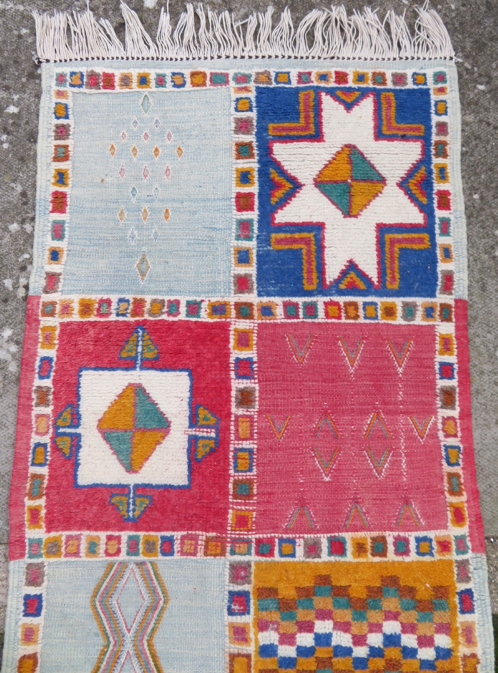 An extra long and narrow handwoven Moroccan Berber runner rug featuring geometric panels in pink, light blue, yellow, and navy with fringed ends. View III