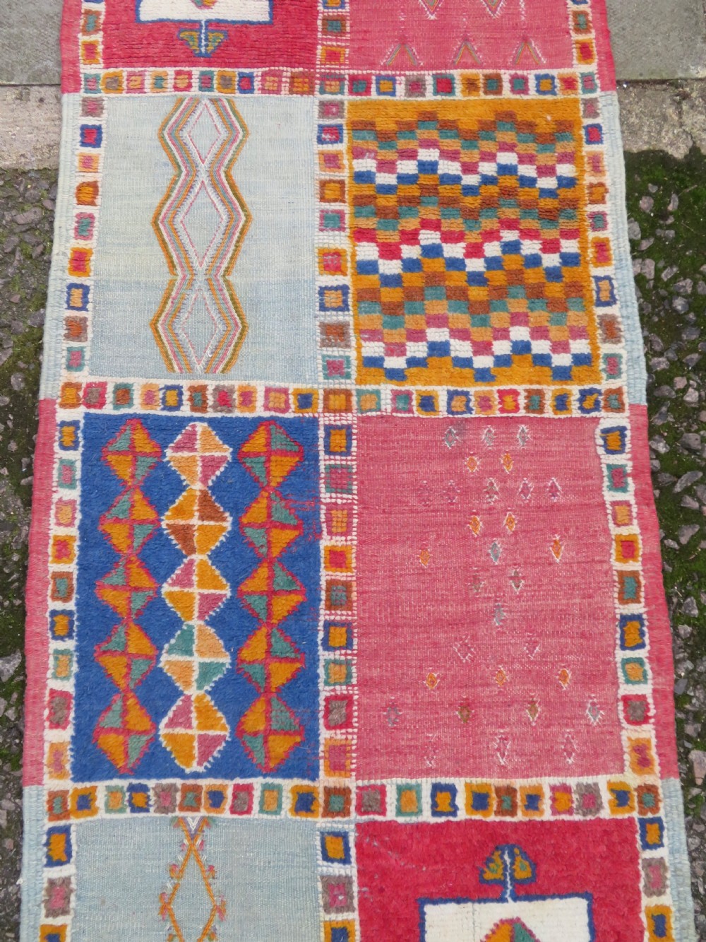 An extra long and narrow handwoven Moroccan Berber runner rug featuring geometric panels in pink, light blue, yellow, and navy with fringed ends. View V