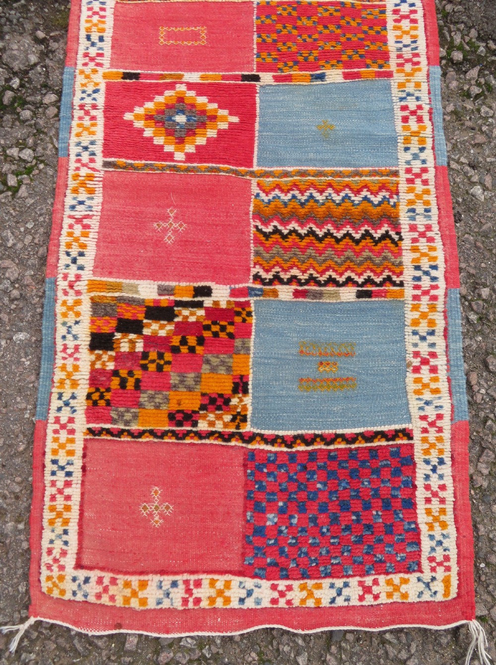 An extra long and narrow handwoven Moroccan Berber runner rug featuring geometric panels in pink, light blue, yellow, and navy with fringed ends. View X