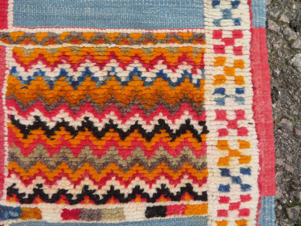 An extra long and narrow handwoven Moroccan Berber runner rug featuring geometric panels in pink, light blue, yellow, and navy with fringed ends. View XII