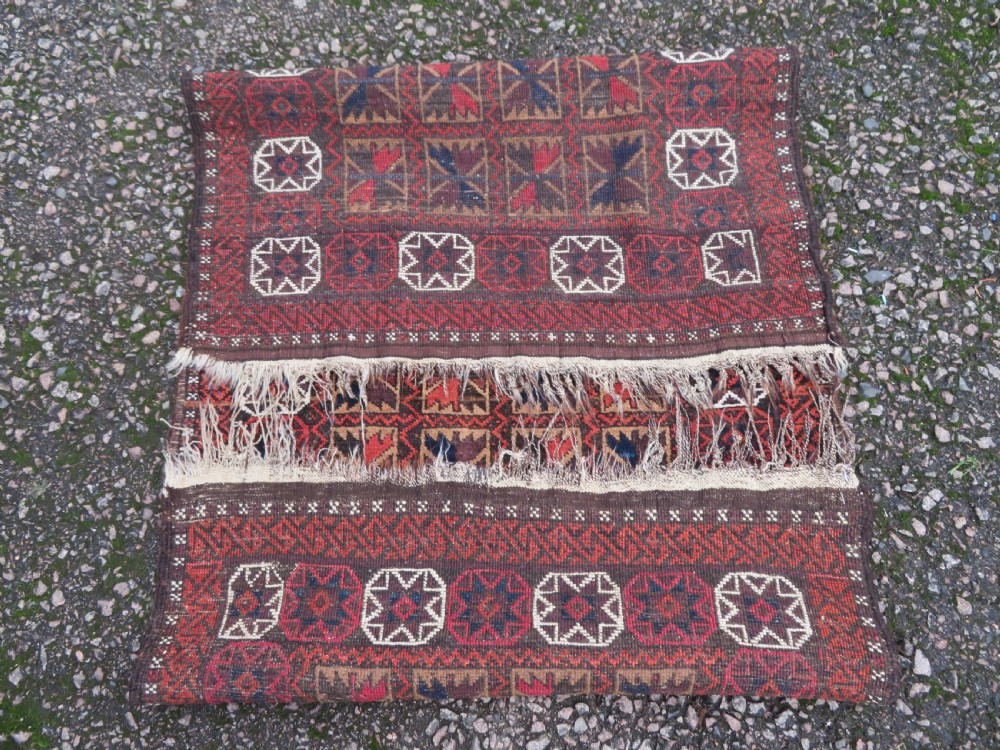 An antique Baluch wool rug featuring a repeating grid pattern of geometric motifs in rust red, dark blue, brown, and ivory accents with a fringed border. View XIV